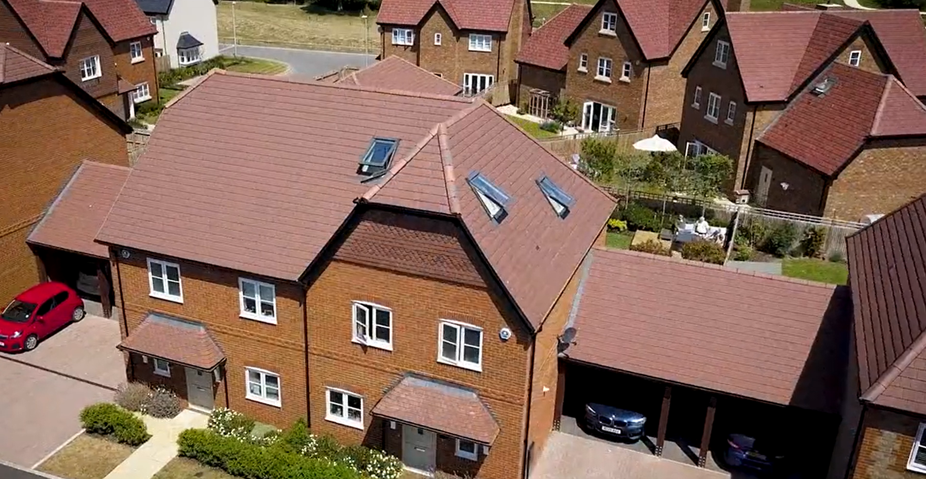 Aerial view of a residential brick home with pitched roof and surrounding houses.
